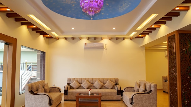 A living room with a sofa, two armchairs, a coffee table, and a decorative ceiling light. - Hotel Ultra International (Siddharthanagar)