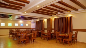 A spacious room with wooden ceiling beams, multiple tables and chairs, and a large window with curtains. - Hotel Ultra International (Siddharthanagar)
