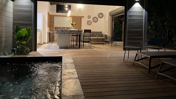 Un patio esterno moderno con un pavimento in legno, una piccola fontana e un'area pranzo con tavolo e sedie.