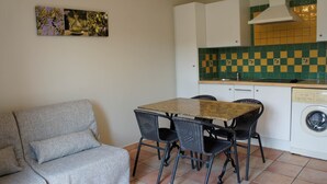 Um espaço compacto com sofá, mesa de jantar, cadeiras, máquina de lavar e painel de azulejos.