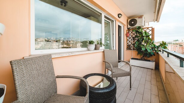 A balcony with wicker chairs, potted plants, and a view of the cityscape. - Bright studio in Trastevere/ ponte Testaccio (Roma)