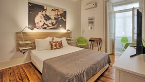 A bedroom with a large bed, a desk, a chair, a painting on the wall, and a window.