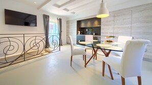 A modern dining area with a glass table, white chairs, and a kitchen in the background. - BASTINICA KRK Superior Ap 3, OldTown, CityCenter (Krk)