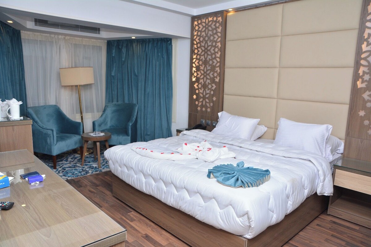 Habitación de hotel con una cama grande, un escritorio con lámpara, una silla y un panel decorativo en la pared.