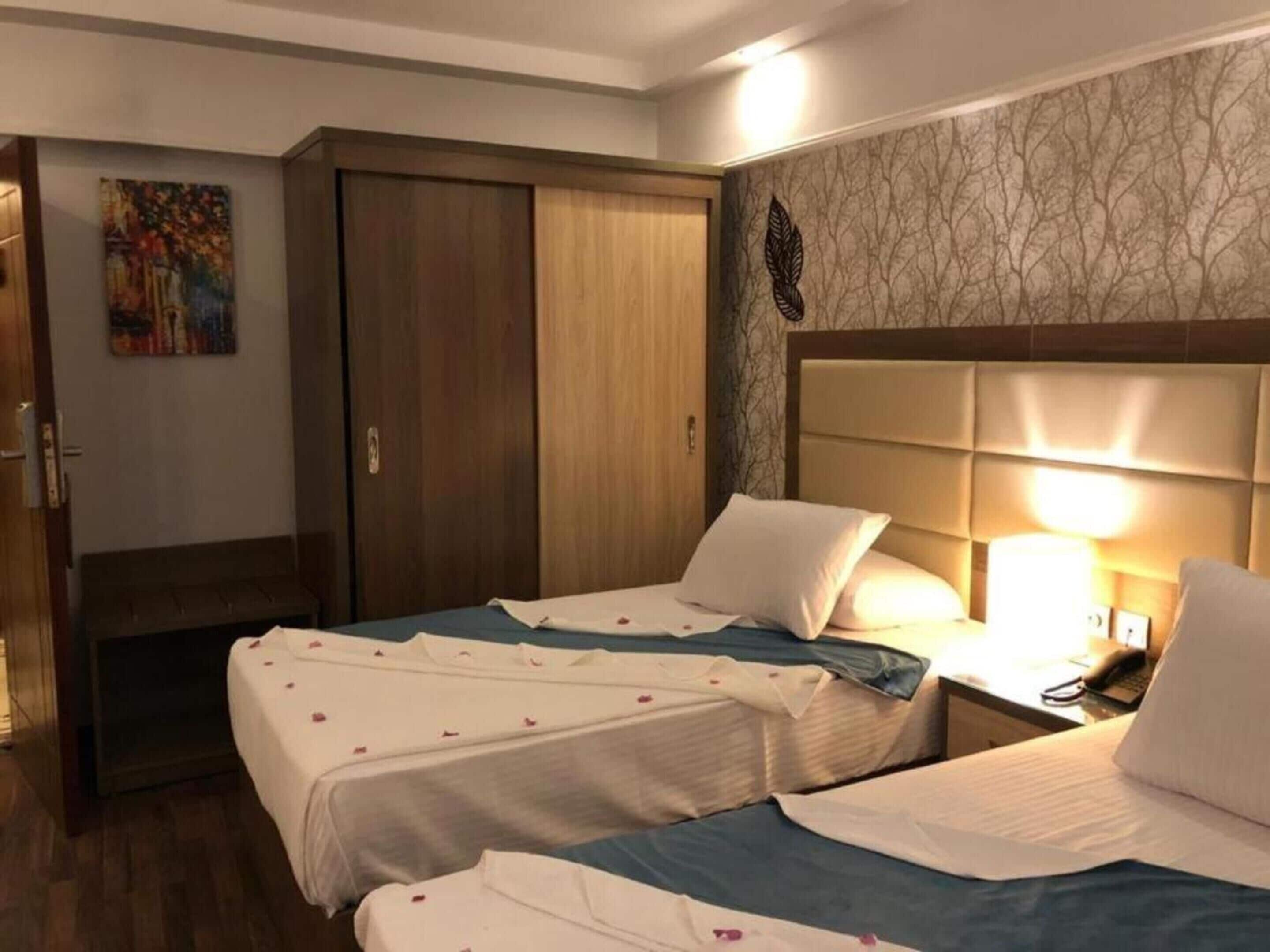A hotel room with two beds, a wooden wardrobe, a painting on the wall, and a patterned wallpaper.