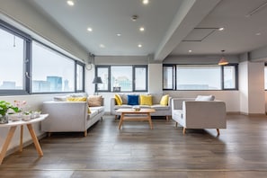 A spacious living room with large windows, a grey sofa set, a wooden coffee table, and a small side table with plants.