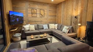 Ein modernes Wohnzimmer mit einer Eckcouch, einem flachbildfernseher an einer Holzwand und einem Kamin.