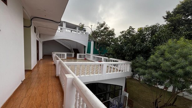 A balcony with a white railing, a wooden floor, and a view of a garden and trees. - Sewadham Training Centre (Phulpur)