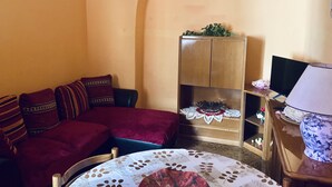A cozy living room with a sofa, a small table with a lace tablecloth, a cabinet with decorative items, and a television. - Delightful little room Near Colosseum!!! (Roma)
