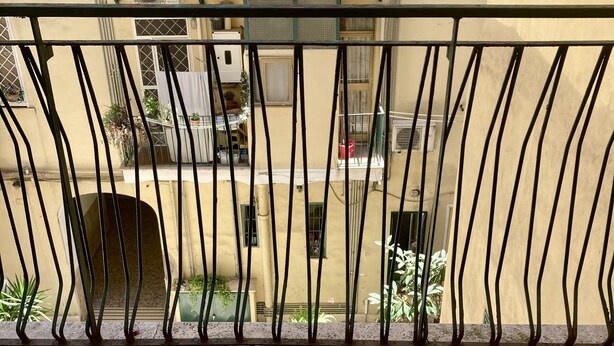 A balcony with a tiled floor, a metal railing, and a view of a building with multiple windows and balconies. - Delightful little room Near Colosseum!!! (Roma)