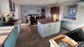 A modern kitchen with wooden cabinets, a central island, and a dining area with chairs. - Spacious Ty Adeiladwr Cwch, with stunning mountain views near Red Wharf Bay (Llanddona)