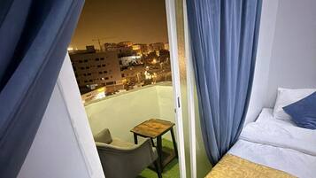 Habitación de hotel con cama, una silla, una mesita y vista a la ciudad de noche.