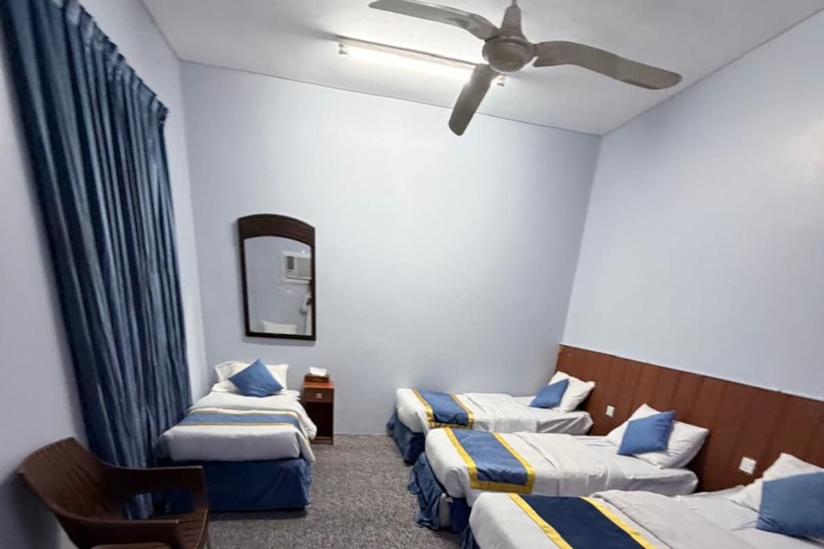 Habitación de hotel con cuatro camas individuales, un ventilador de techo, un espejo y una silla.