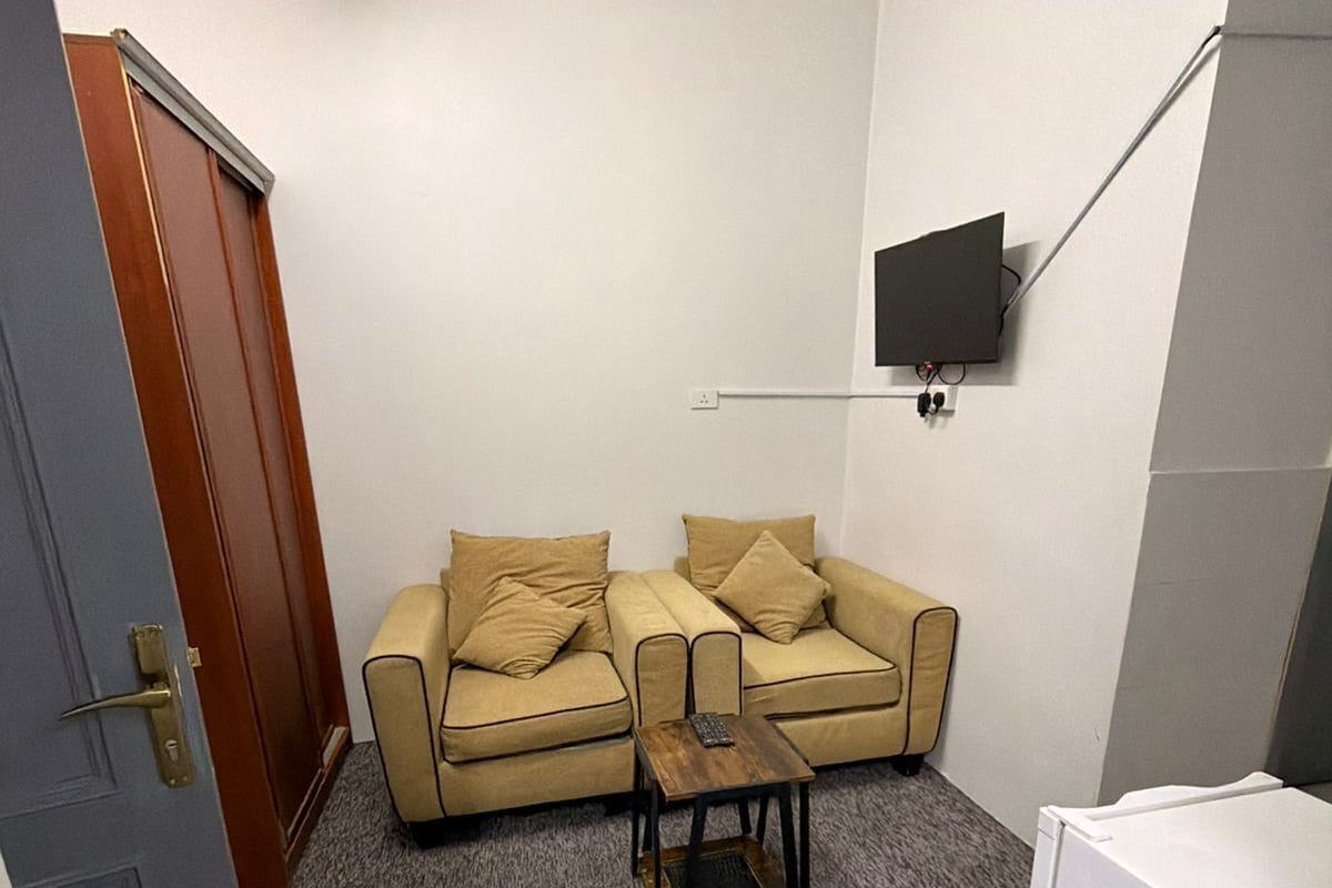 Una habitación pequeña y funcional con un sofá, una mesita, un televisor fijado a la pared y una puerta.