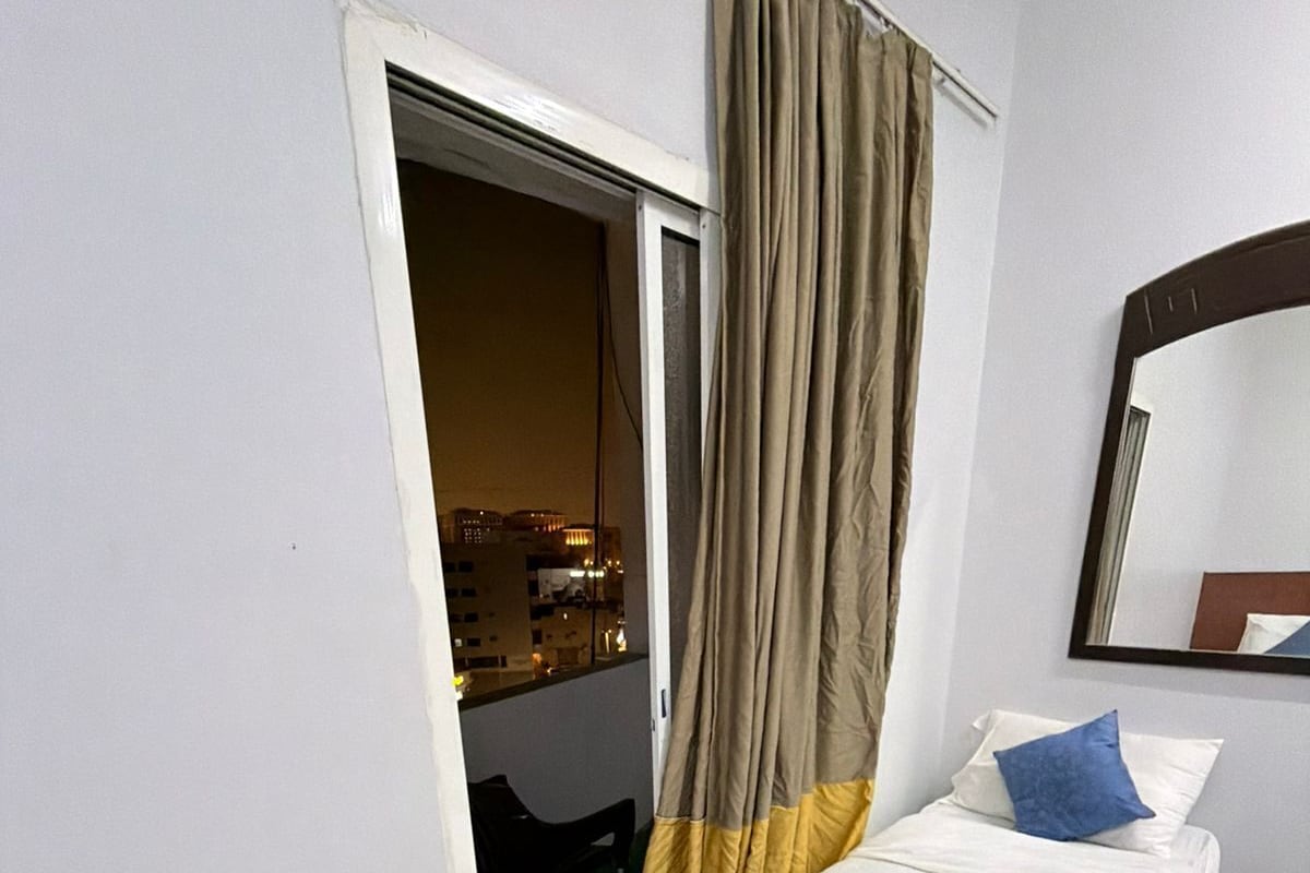 Habitación de hotel con cama, una silla, un espejo y vista a la ciudad a través de la ventana.