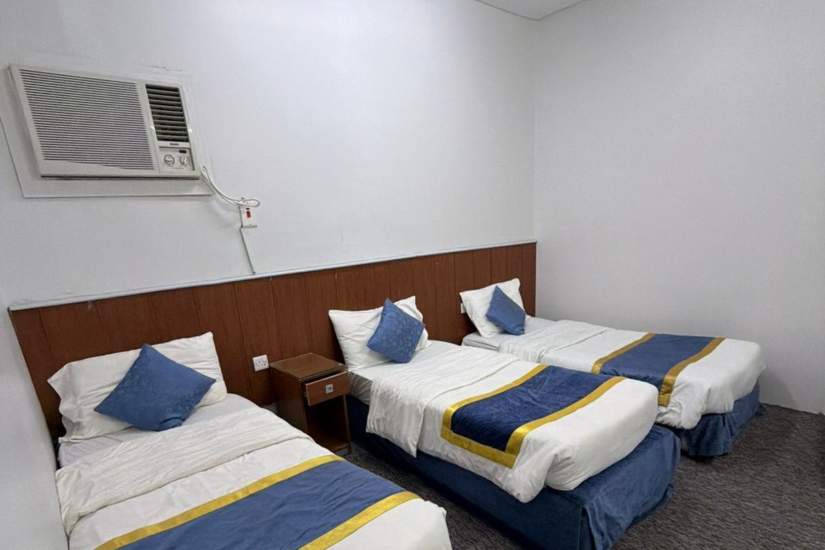Habitación de hotel con tres camas individuales, cabecera de madera, mesita de noche y aire acondicionado instalado en la pared.