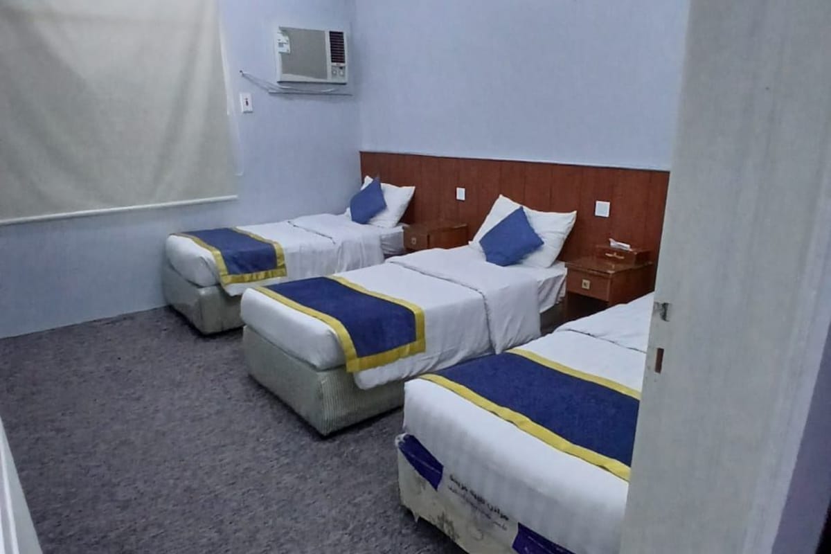 Habitación de hotel con dos camas, ventilador de techo, equipo de aire acondicionado y extintor.