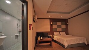 A hotel room with a bed, bedside table, and a bathroom with a sink and shower. - Equus Motel (Jincheon)