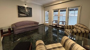 A spacious living room with a black marble floor, a ceiling fan, and a large window with a view of the outside. There are two sofas and a coffee table. - Brham Store and Residency Brunton Road  (Bengaluru)