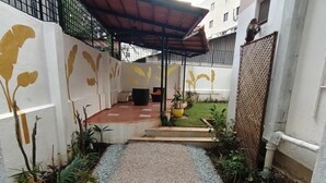 A narrow pathway leading to a covered seating area with a small garden and potted plants. - Brham Store and Residency Brunton Road  (Bengaluru)