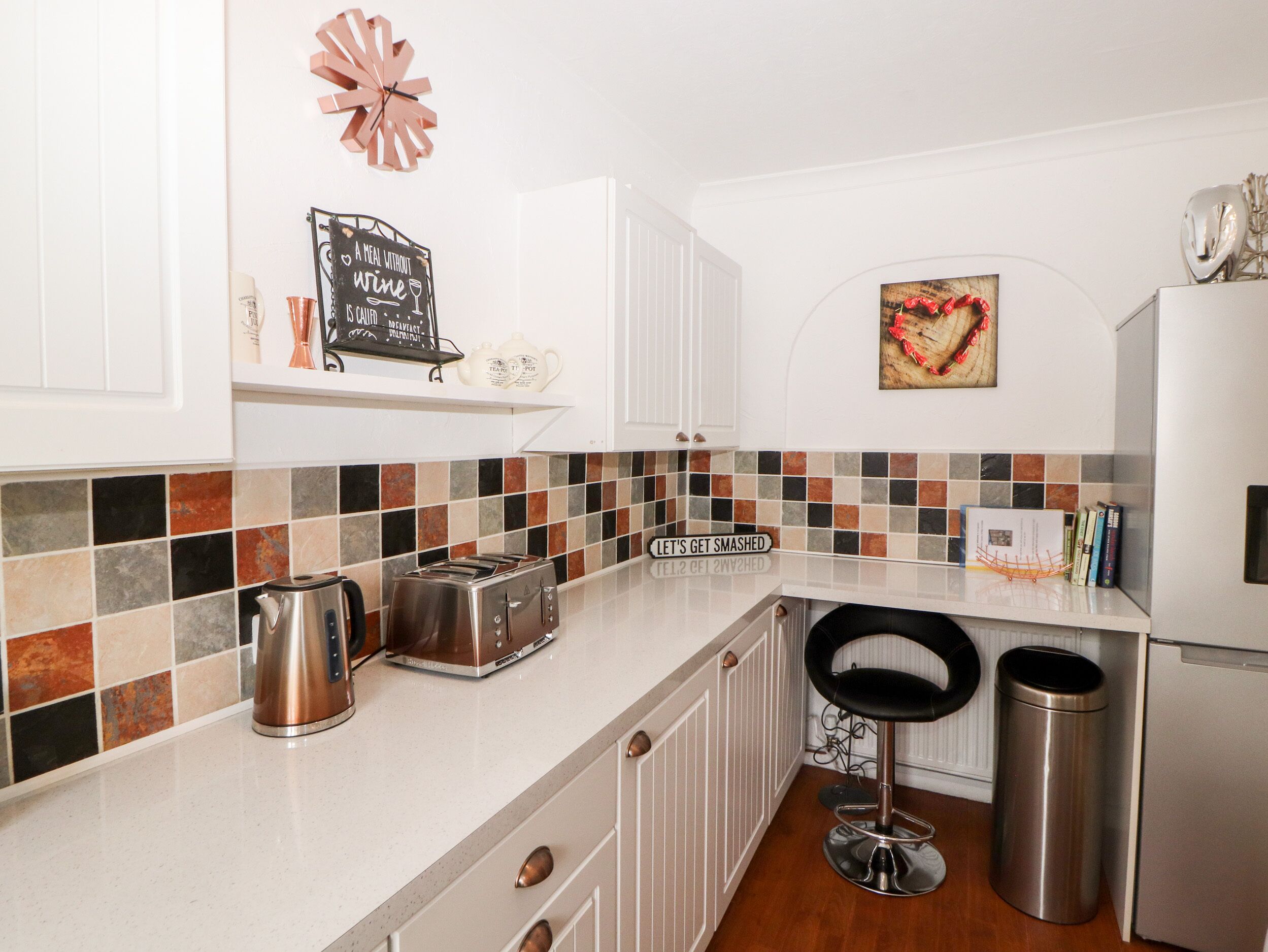 Eine moderne Küche mit weißen Schränken, einer gefliesten Spritzschutzwand, einem Toaster, einem Wasserkocher und einem Mülleimer.