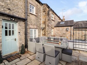 A stone building with a light blue door, a small porch with wicker furniture, and a metal gate. - Market Square Maisonette (Carnforth)