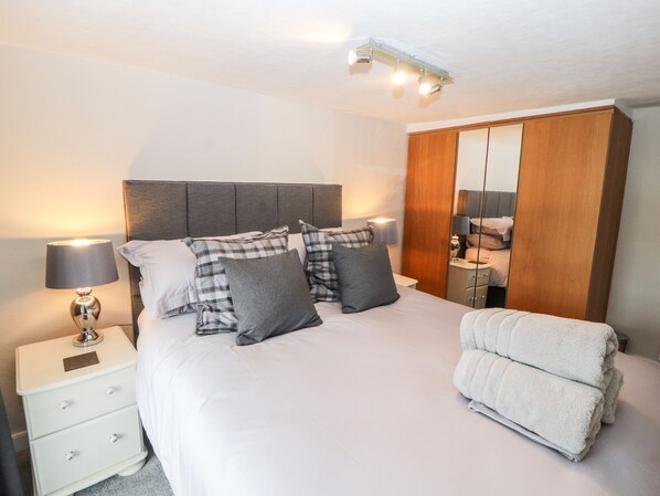 A neatly made bed with a grey headboard, a bedside lamp, and a mirror cabinet.