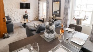 Een moderne woonkamer met een bank, een eettafel gedekt voor twee personen, een open haard en een grote spiegel.