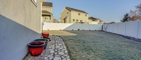 A residential backyard with a stone pathway, potted plants, and a white fence.