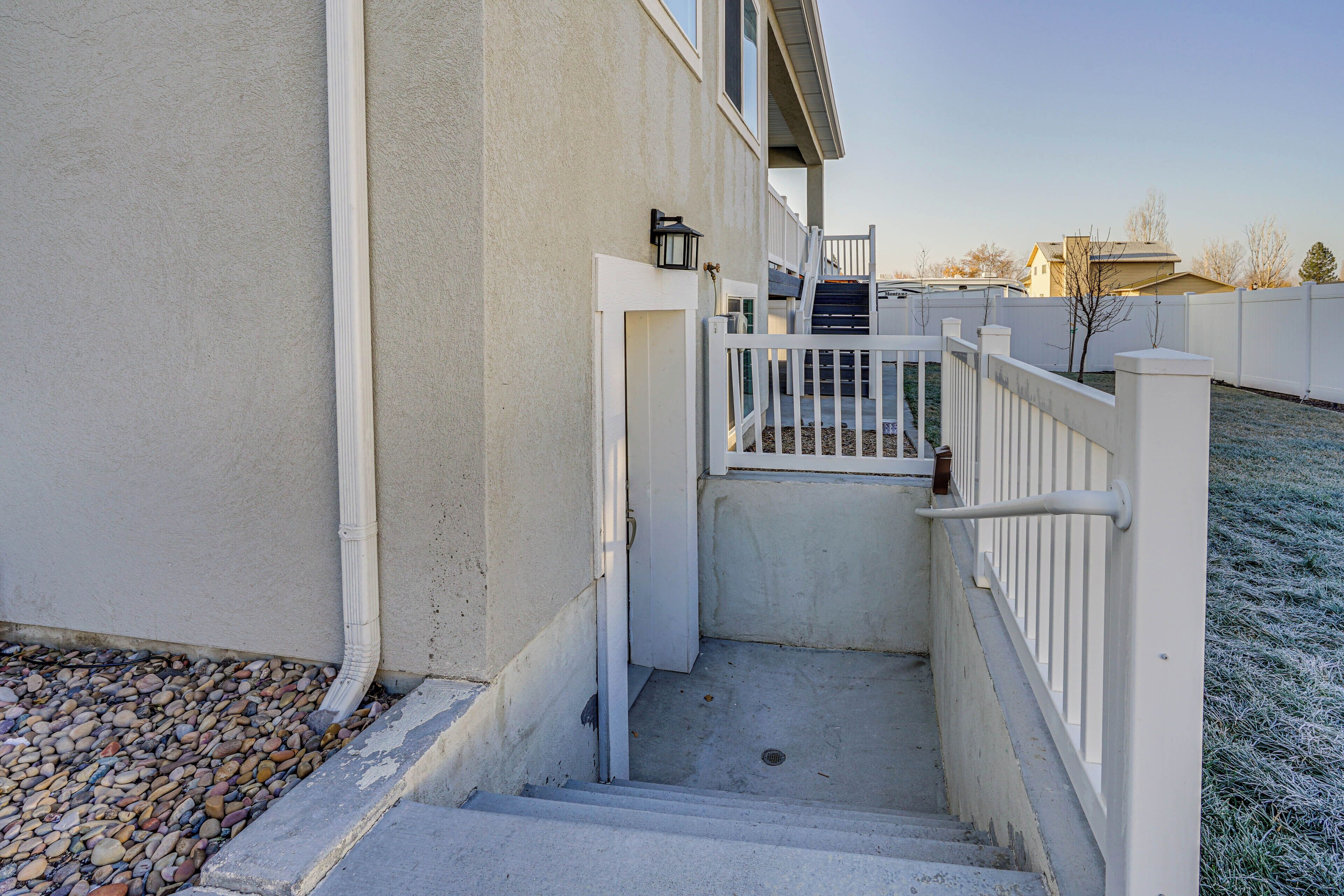 A set of concrete steps leading up to a white metal gate, with a small black lantern on the wall to the left.