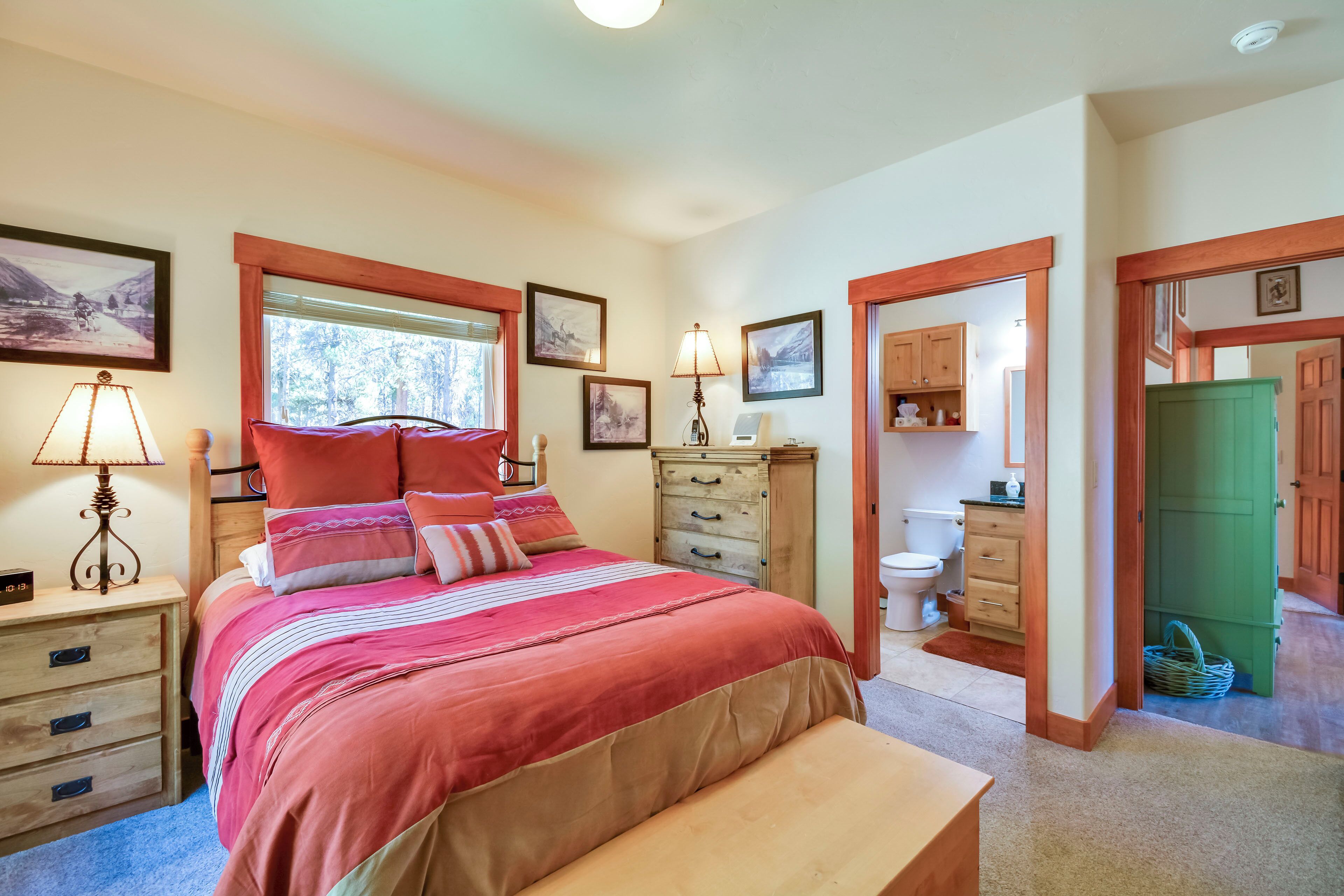 A bedroom with a large bed, wooden nightstands, a dresser, and a green door leading to the bathroom.