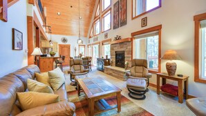 A spacious living room with a high ceiling, large windows, a fireplace, leather furniture, and a stone fireplace surround. - Quiet Leadville Home on 3 Acres w/ Gas Grill! (Leadville)