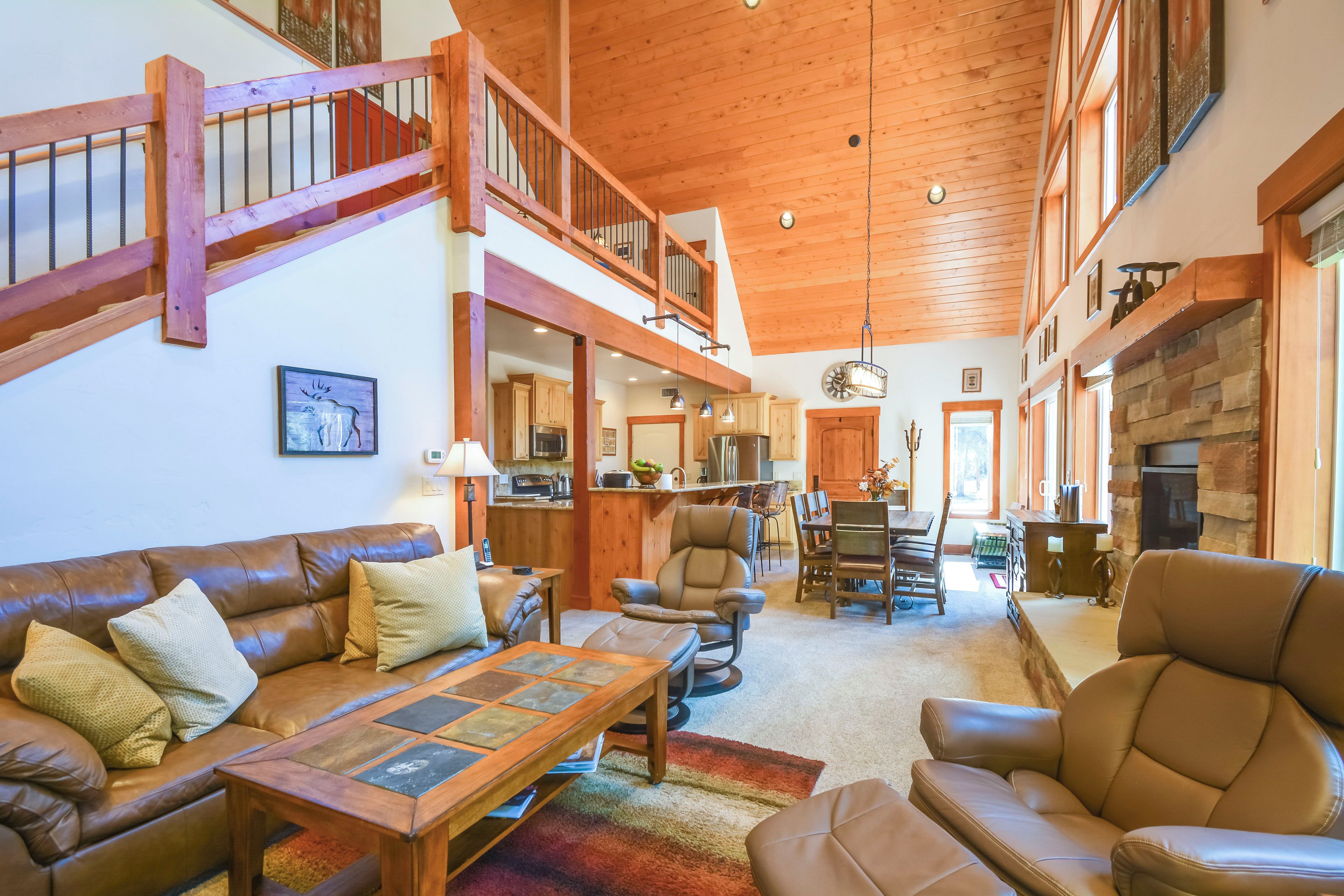 A spacious living area with a high ceiling, wooden staircase, and a kitchen in the background.