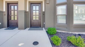 A building entrance with two brown double doors, a small landscaped area with green shrubs, and a concrete pathway leading to the door. - Stunning Mtn Views! Home 3 Mi to Dtwn Cedar City! (Cedar City)