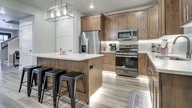A modern kitchen with wooden cabinets, stainless steel appliances, and a central island with bar stools. - Stunning Mtn Views! Home 3 Mi to Dtwn Cedar City! (Cedar City)