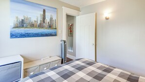 A bedroom with a bed, a desk, a heater, a door, and a painting of a cityscape.