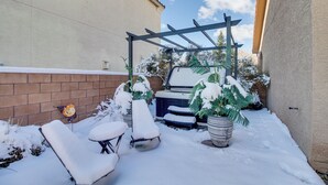 Un patio cubierto de nieve con mobiliario exterior, un jacuzzi y plantas en macetas.