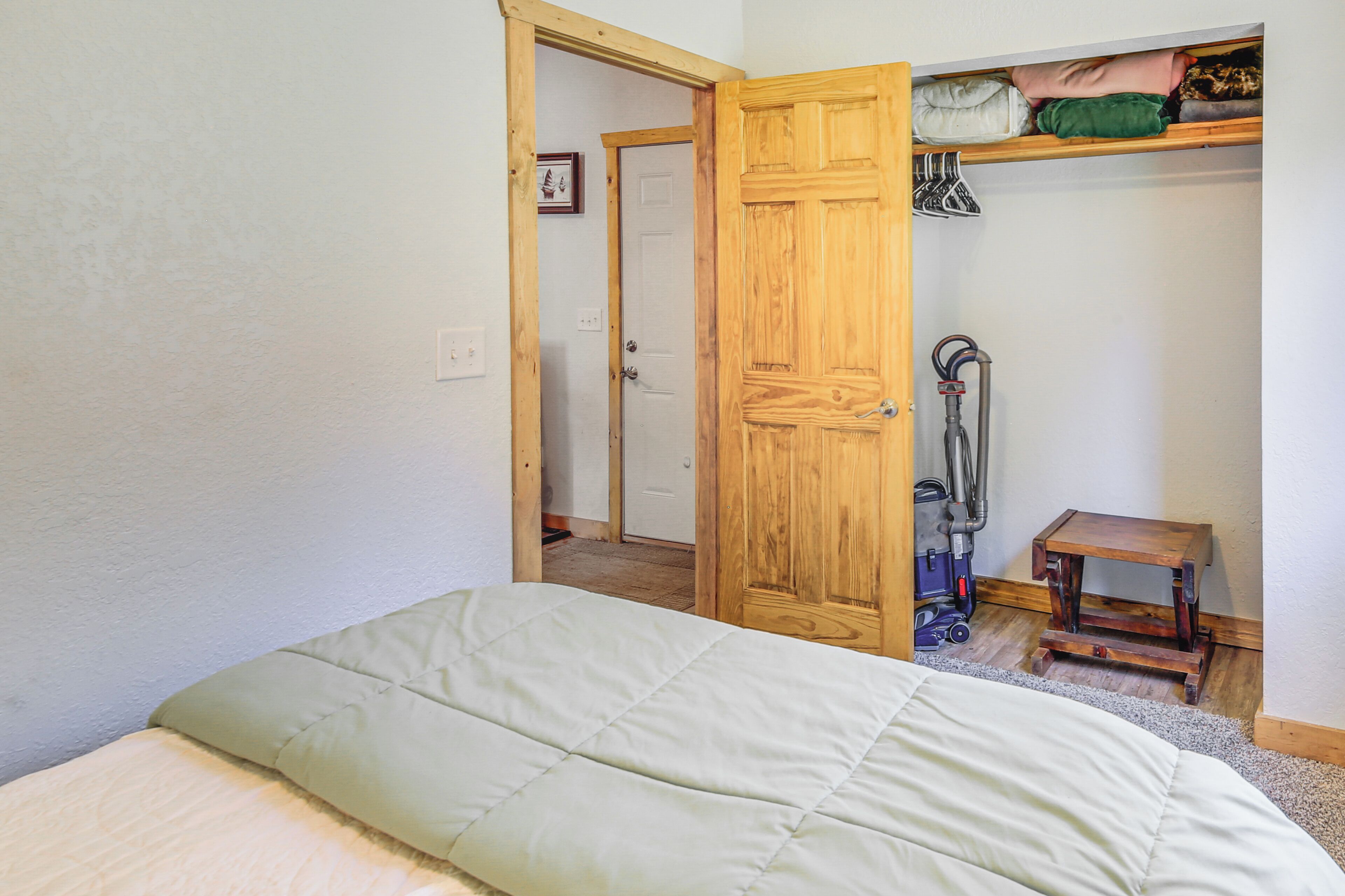 Een slaapkamer met een bed, een houten garderobe, een stofzuiger en een klein houten tafeltje.