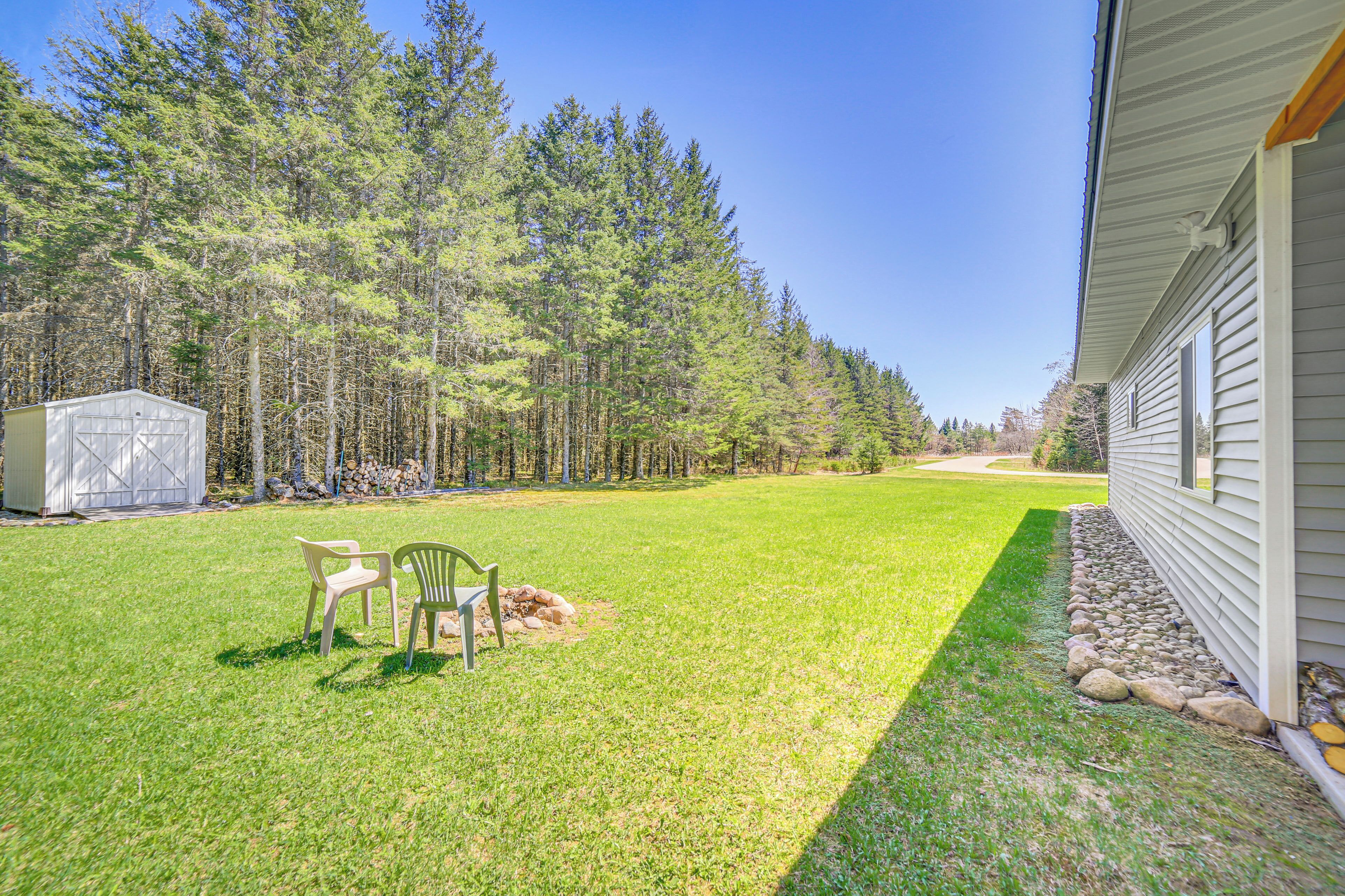 A backyard with a lawn, two chairs, a shed, and a house.