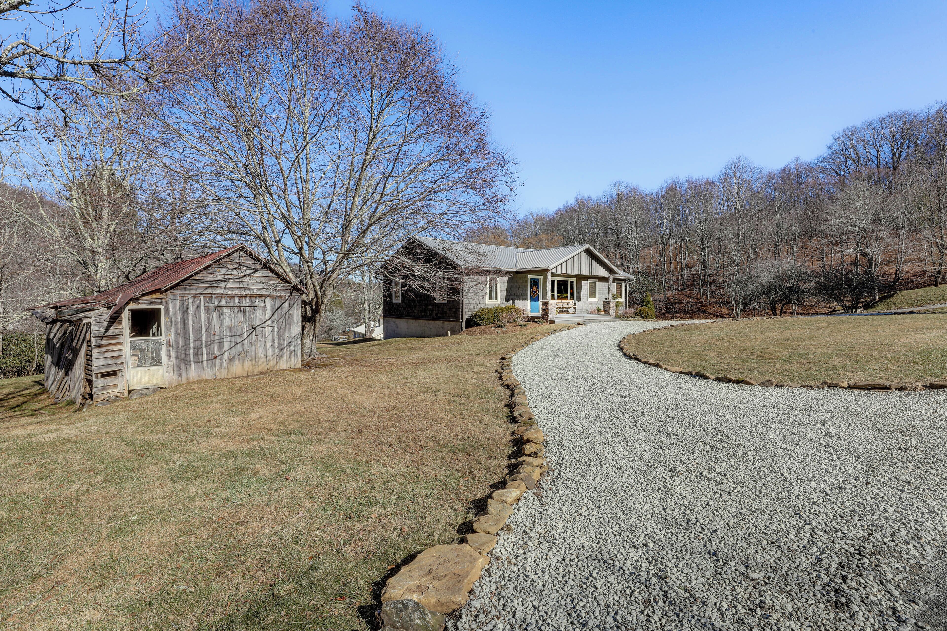 A rural property with a gravel driveway, a wooden barn, and a house with a blue door.