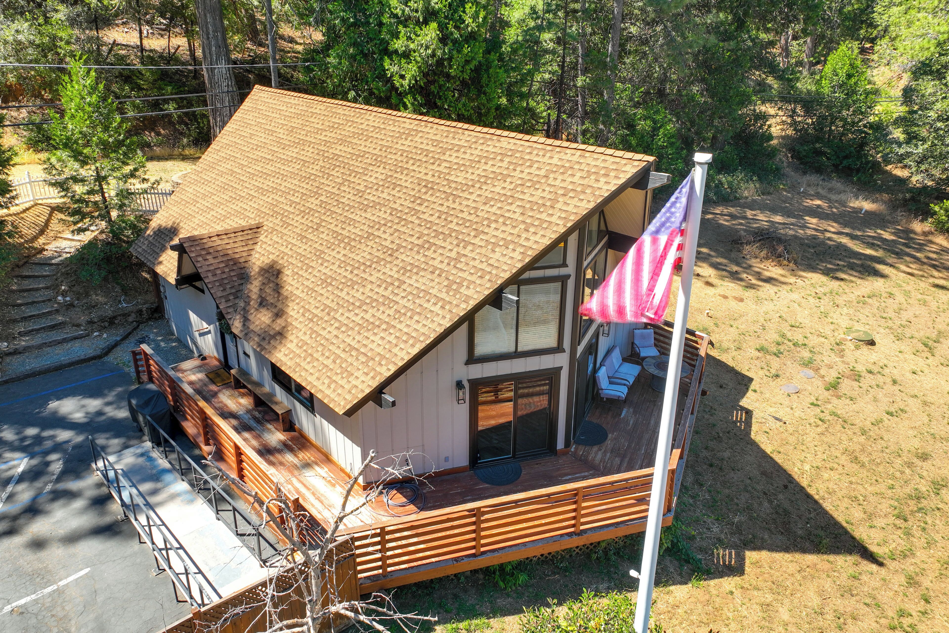 A two-story cabin with a sloped roof, a deck with seating, and an American flag.
