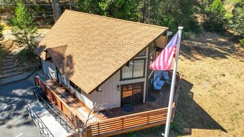 A two-story cabin with a sloped roof, a deck with seating, and an American flag.