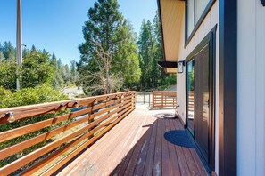Une terrasse en bois avec une balustrade, un bâtiment doté de grandes fenêtres et une vue sur des arbres et une route.