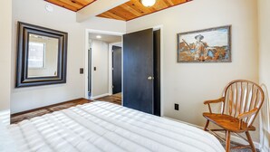 Un dormitorio con una cama grande, una mecedora de madera, un cuadro en la pared y una puerta que da a otra habitación.