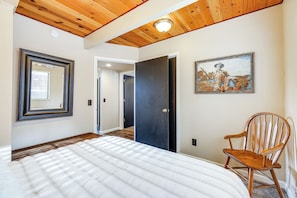 Un dormitorio con cama, techo de madera, un cuadro y una silla.