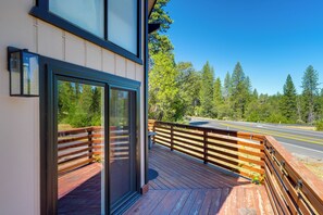 A wooden deck with a glass door leading to a room, overlooking a road and forest. - Serene Cabin Retreat Between Murphys & Arnold (Murphys)