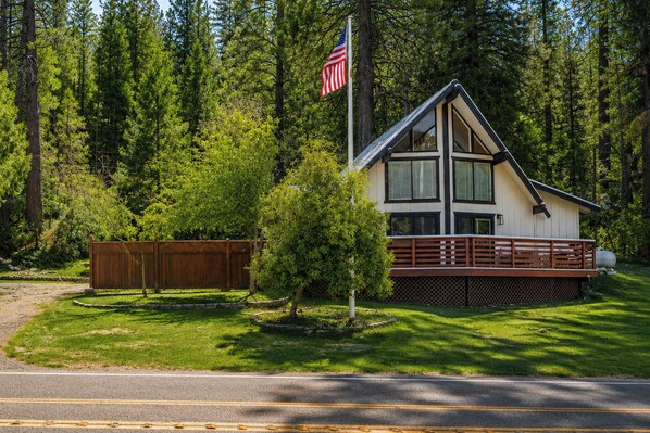 A cabin with a deck, surrounded by trees and a flag. - Serene Cabin Retreat Between Murphys & Arnold (Murphys)