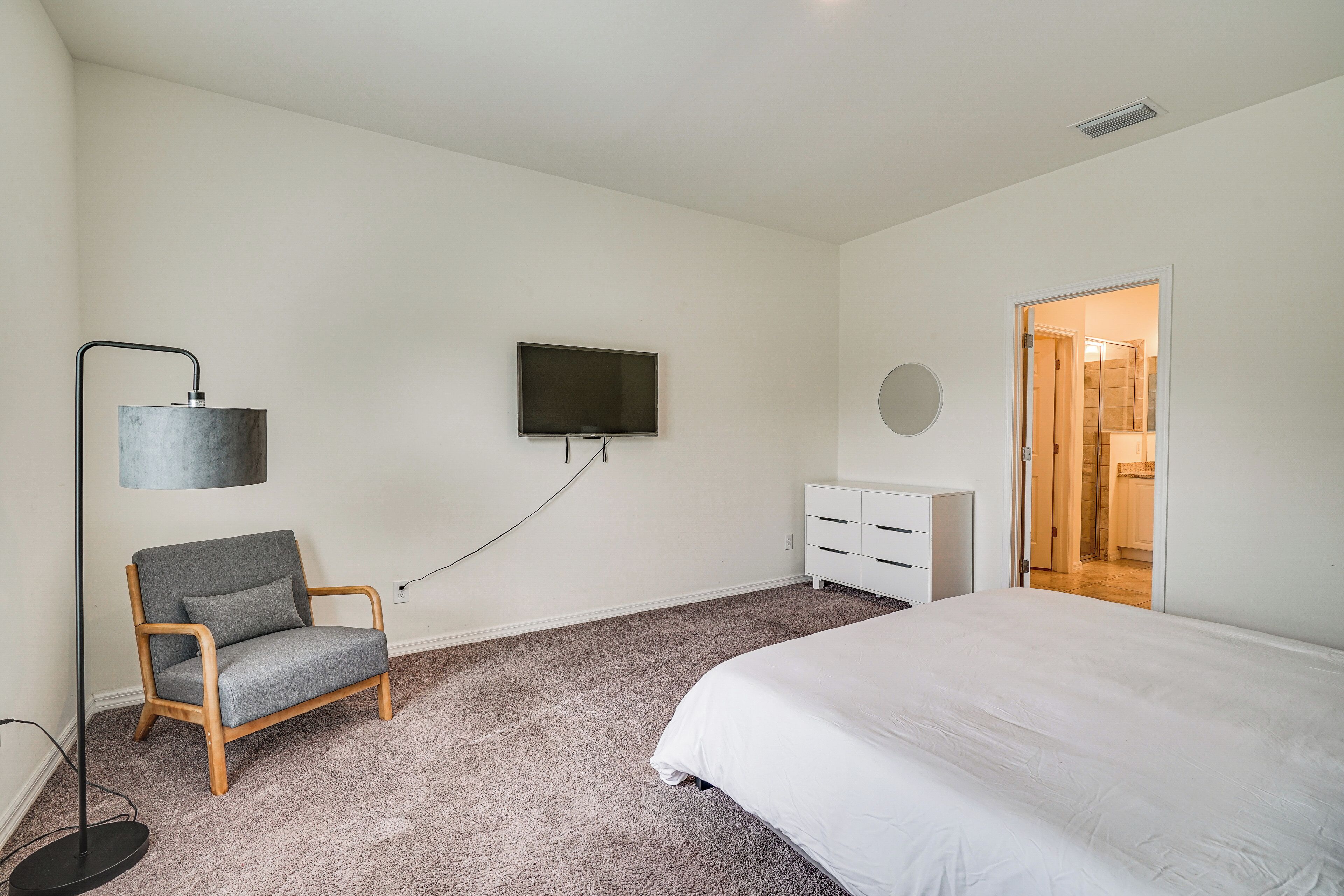 Quarto com cama, cadeira, televisão, penteadeira e porta que dá para um banheiro.