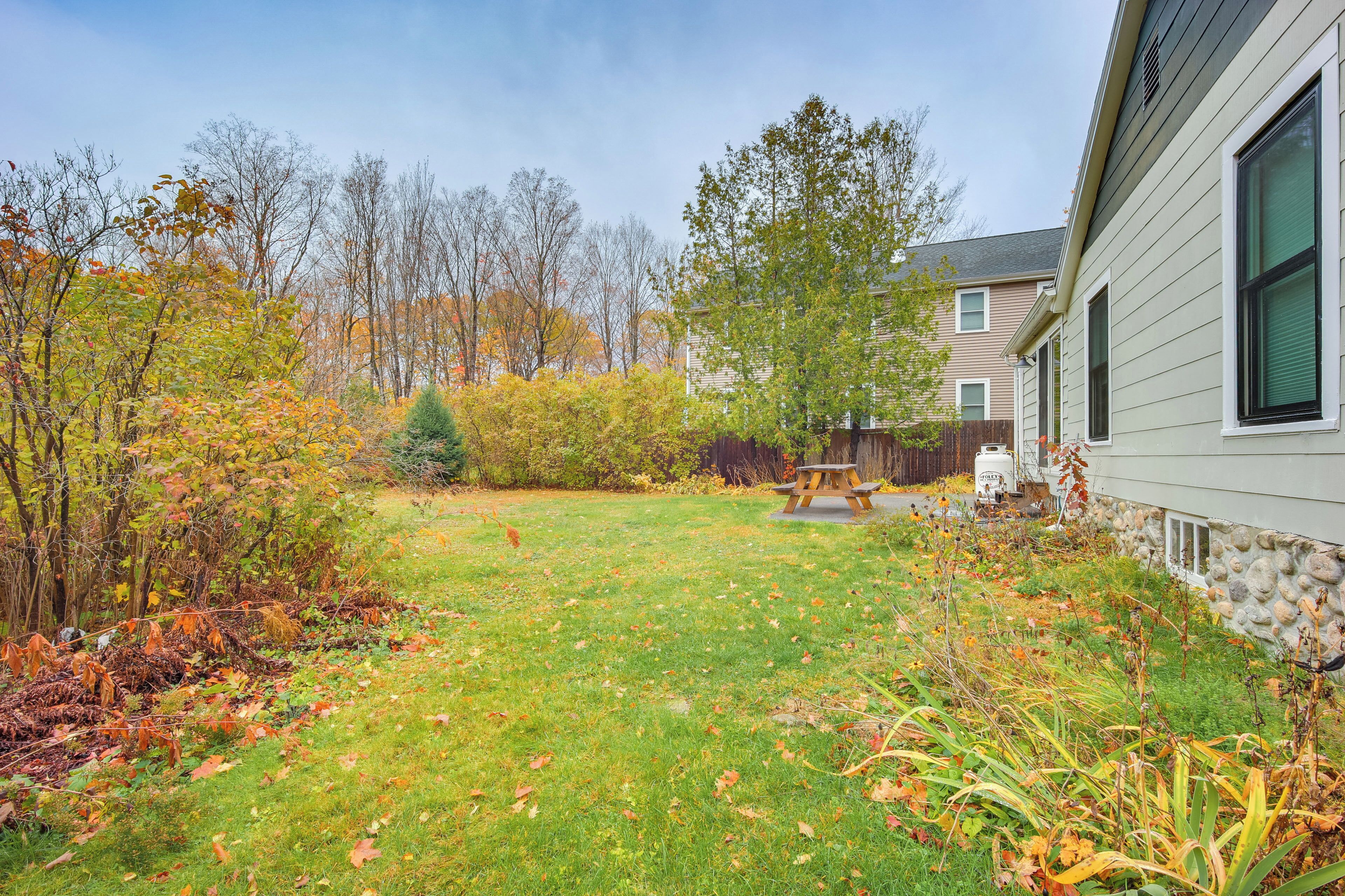 A residential yard with a picnic table, a stone wall, and a variety of trees and shrubs.