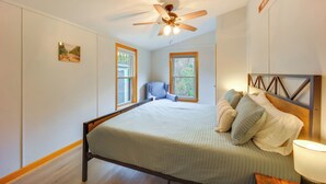 A bedroom with a bed, a ceiling fan, two windows, a chair, and a nightstand with a lamp. - Comfortable Lincoln Home: Walk to Main Street! (Lincoln)